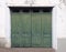 Old wooden paneled exterior doors with green fading cracked paint in a white frame and distressed white wall