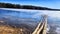 An old wooden pier on the shore of a lake with ice in early spring on a sunny day. Freezing lake in autumn and wooden