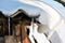 Old wooden planks wall of henhouse with rusty nails covered with white snow on roof and icicle, grunge background texture