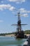 An old wooden ship with high masts. The ship is off the coast.