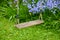 Old wooden swing in a garden with blue flowers and moss growing in backyard. Peaceful scene of a forgotten playground