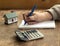On an old wooden table is a calculator, a small house, a notebook and a pen. The concept of buying, selling real estate