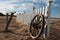 An old wooden wagon wheel leans against a wooden fence.