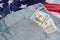 Old worn jeans are lying on flag United States America and there are hundred dollar bills in pocket