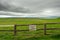 Old worn warning sign `Private property` on a fence by a green field, Grey cloudy sky,