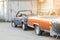 Old wrecked covered car at back yard of workshop. Abandoned convertible vehicle under black curtain near garage doors. Recycling a