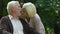 Old wrinkled man and woman kissing with tenderness in park, happiness and love