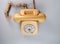 Old yellow antique rotary telephone on blue background. Vintage landline home phone with dial, twisted cable and