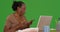 An older black woman works on her laptop with her paperwork on green screen
