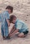 Older brother kneels down in sand to help his toddler brother with shoes