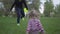 Older brother and small sister run in beautiful green park. Small girl fall down and boy help her to stand up. Happy