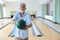 Older caucasian men, white beard and white hair in white and blue shirt playing bowling while he holding bowling ball to someone