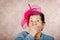 Older cute hispanic woman wearing blue sweater, large pink ribbon on head loking into camera covering her mouth with one