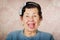 Older cute hispanic woman wearing blue sweater and polka dot bowtie on head showing her tongue to the camera in front of