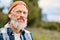 Older elder hipster man standing in nature park wearing earbud. Portrait