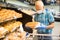 Older european man wearing mask and gloves with covid protection chooses buns and bread in supermarket bakery