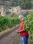 Older farmer in a vineyard with a ruined monastery in the background, looking at his cell phone