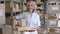 Older female entrepreneur holding parcel boxes in warehouse, portrait.
