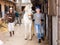 Older female stable keeper leading horse outdoors while Asian woman carrying saddle