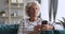 Older grey-haired grandma using mobile apps sit on sofa