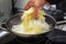 Older hand is laying celery strips in a wok pan with boiling oil