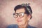 Older hispanic cute woman with flower pattern bow on her head wearing blue sweater and black large framed glasses