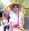 Older latin woman with protective face masks and hat walking in plaza, new normal covid-19