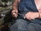 Older man has on dark navy working clothes is sitting at the workbench in workshop. Blurred background, soft selective