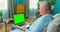 Older Man at Home Sitting on a Couch Works on a Laptop Computer with Green