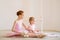 The older sister, a ballerina in a pink tutu and pointe shoes, shows the baby how to practice at the barre