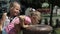 The older sister helps the younger one drink water from the fountain