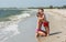 The older sister hugs her younger brother on the beach with waves and sea foam, happy children.