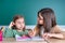 Older sister looks at her younger sister as she draws in a notebook