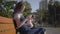 Older sister with younger brother sitting on the bench in the summer park. The boy unsuccessfully trying to take away