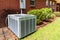 Older style air conditioner system next to home, brick and bushes with clean yard