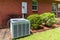 Older style air conditioner system next to home with brick, bushes and clean yard