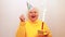 Older woman with a gift wear yellow sweater and horn cap on a white background holding plate with cake with fireworks