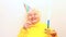 Older woman with a gift wear yellow sweater and horn cap on a white background holding plate with cake with fireworks