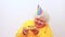 Older woman with a gift wear yellow sweater and horn cap on a white background holding plate with cake with fireworks