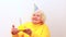 Older woman with a gift wear yellow sweater and horn cap on a white background holding plate with cake with fireworks