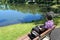 Older woman sits on bench with oxygen tank looking at pond