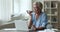 Older woman talks on speakerphones seated at desk with laptop