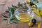 Olive oil dripping in the glass transparent bowl. Canned black and green olives, branches of olive tree on the wooden background