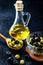 Olive oil in vintage glass bottles with black, green olives and wooden spoon on black background. Copyspace. Flatley. Food