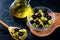 Olive oil in vintage glass bottles with black, green olives and wooden spoon on black background. Copyspace. Flatley. Food