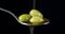 Olives are in a spoon of flowing a stream of olive oil.