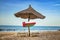 Oman flag on wooden arrow sign. There are two sun loungers and a sun umbrella on the beach. It is a tropical paradise with a clear