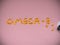 Omega-3 lettering lined with fish oil capsules on pink background.