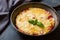 Omelet, scrambled eggs with tomatoes and cheese in a pan on a dark table