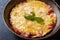 Omelet, scrambled eggs with tomatoes and cheese in a pan on a dark table